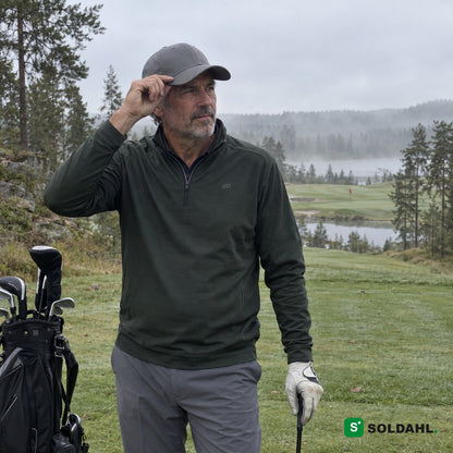 Golfer i grønn genser som justerer en grå caps på en tåkete golfbane