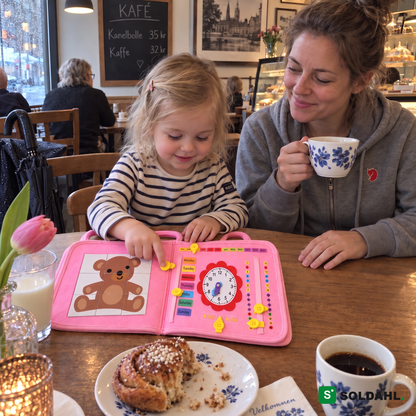 Treåring på kafé knepper i aktivitetsboken mens mamma drikker kaffe