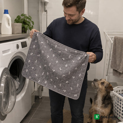 Mann tar den vaskede grå valpematten ut av vaskemaskinen mens hunden ser på